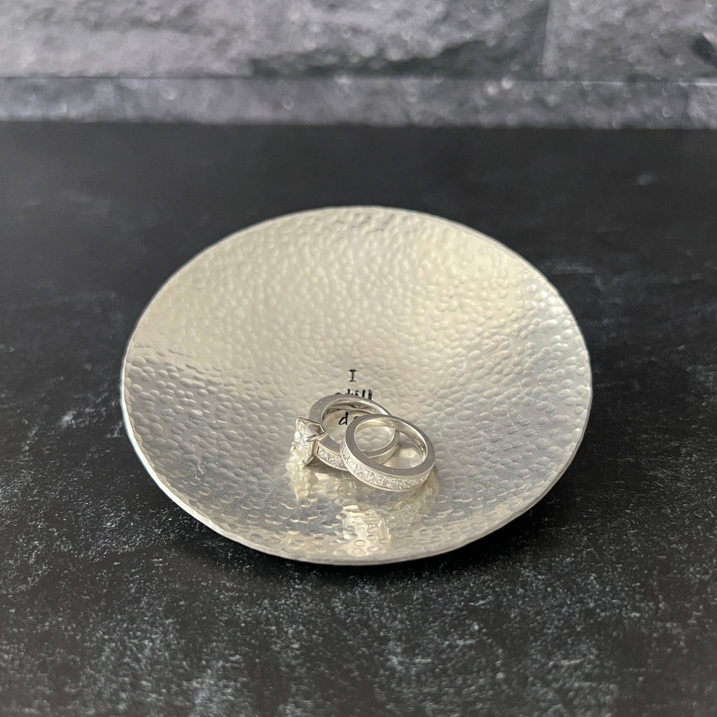 hammered pewter ring dish with a personalized message hand-stamped on the dish. The image shown has I still do in the center. Choose to add your custom text in the center and/or along the top and bottom rim.