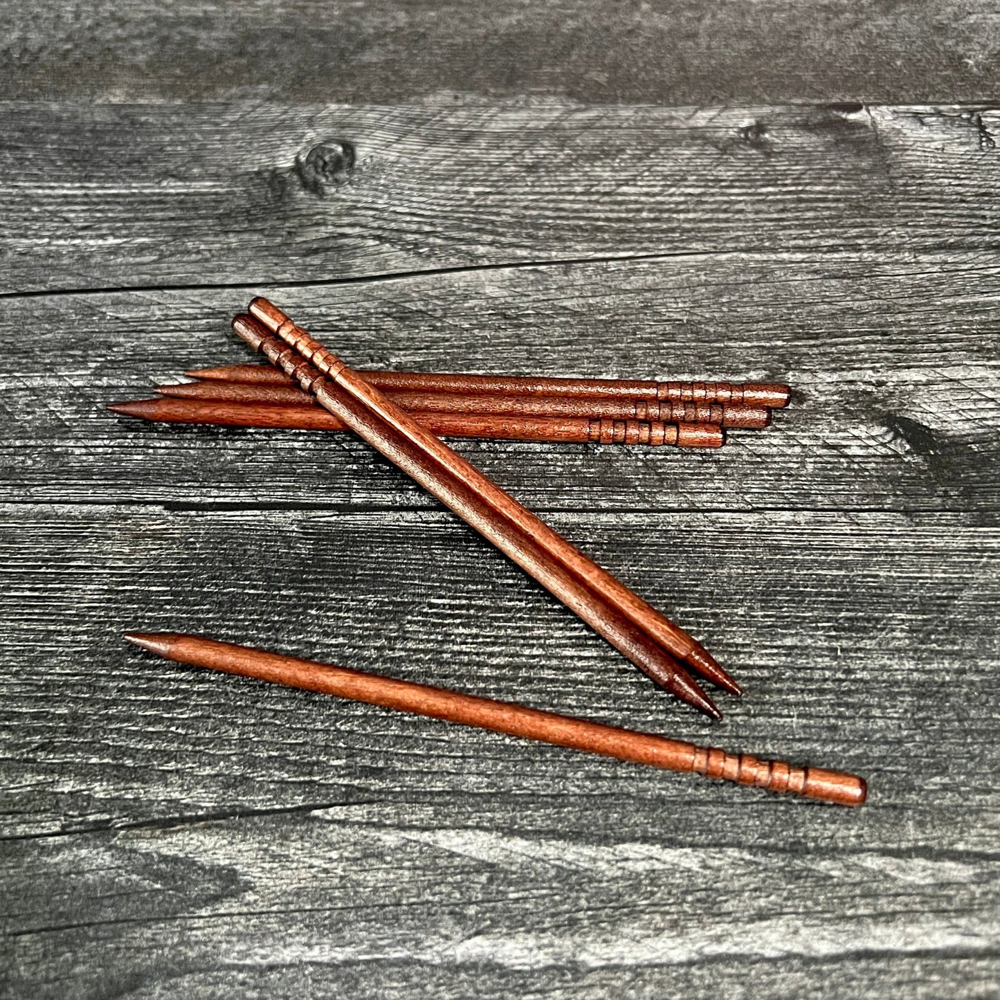 A collection of wooden sticks laid out on a wooden surface, likely used as part of a craft kit for making hair barrettes.