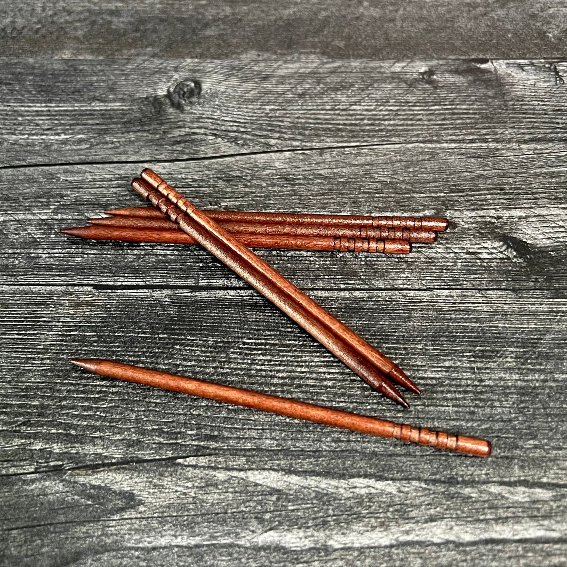 A collection of wooden sticks laid out on a wooden surface, likely used as part of a craft kit for making hair barrettes.