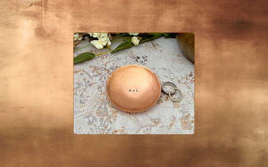 Handcrafted copper ring dish stamped with initials and Roman numeral VII for a 7th anniversary gift, with wedding rings and flowers