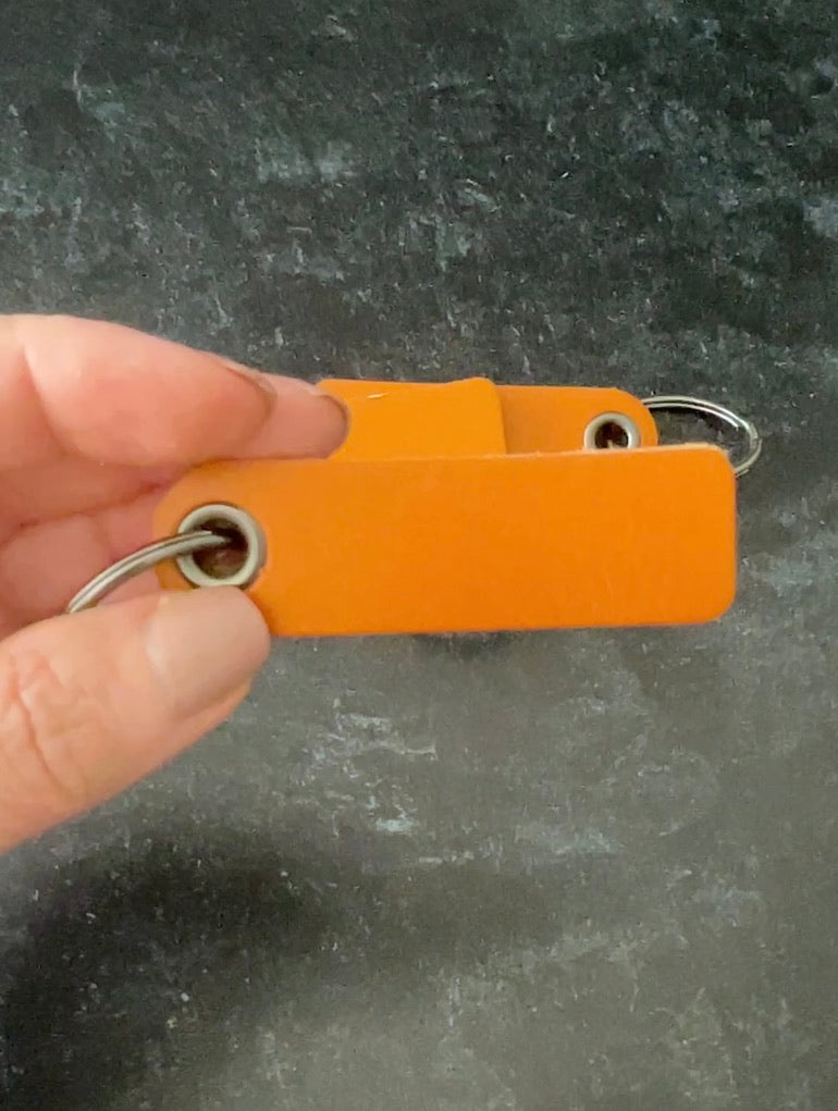 Hand holding an orange leather key fob against a dark gray background