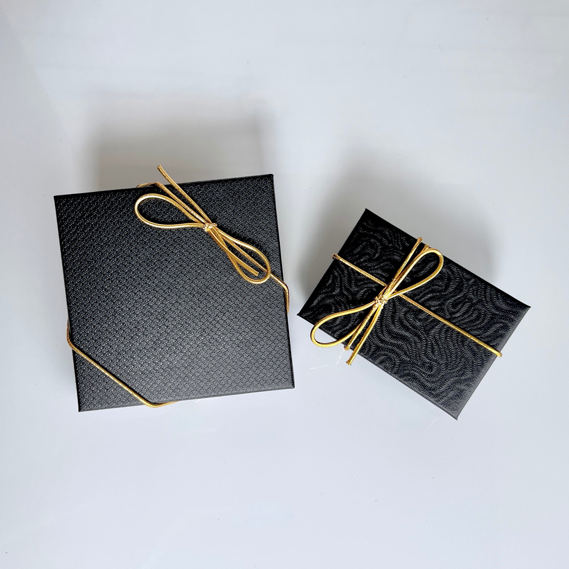 Black textured gift boxes with gold cord bows