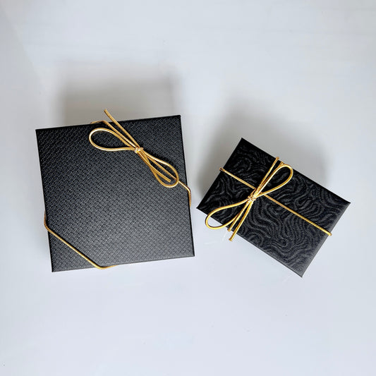 Black textured gift boxes with gold cord bows