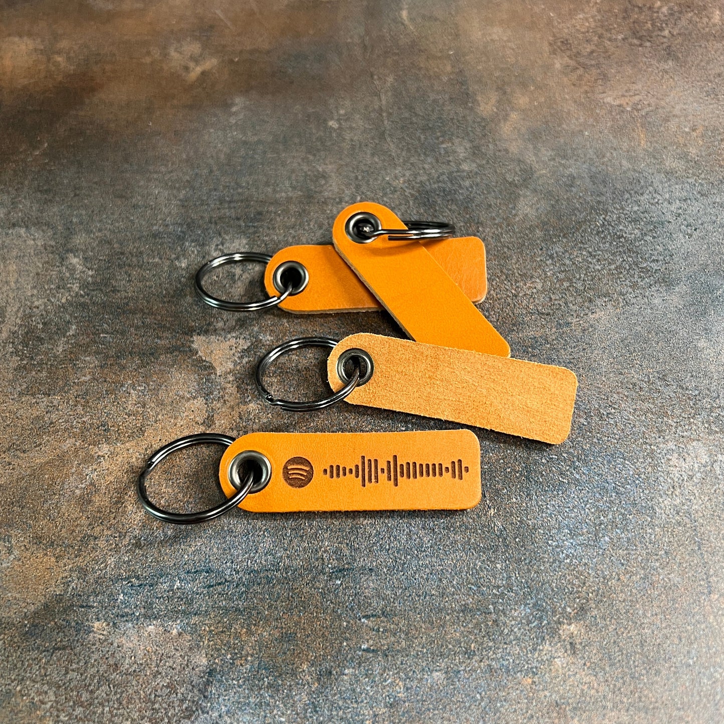 Three brown leather keychains with metal rings on a textured gray surface
