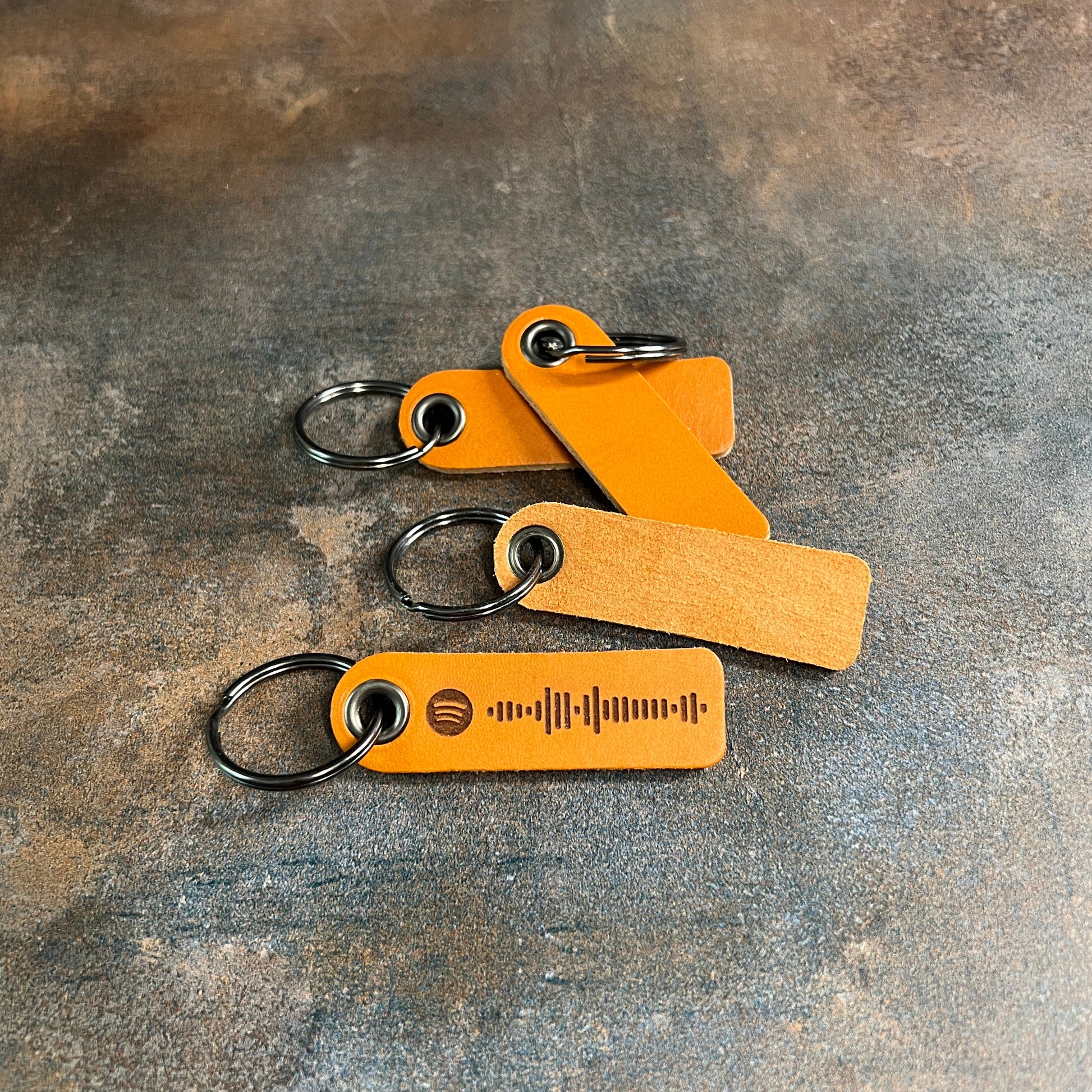Three brown leather keychains with metal rings on a textured gray surface
