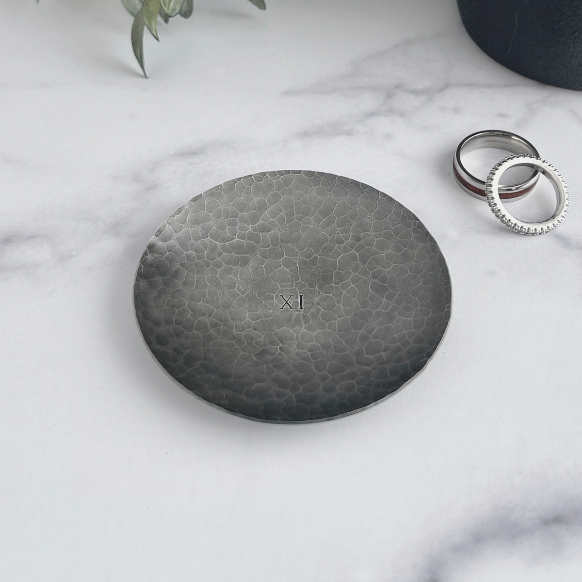 Personalized hammered and darkened steel round ring dish. Dish has 11 in Roman numerals hand-stamped in the center with wedding rings next to the dish.